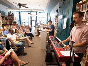 A musician playing in front of a crowd at a Civic Saturday gathering in a bookstore.