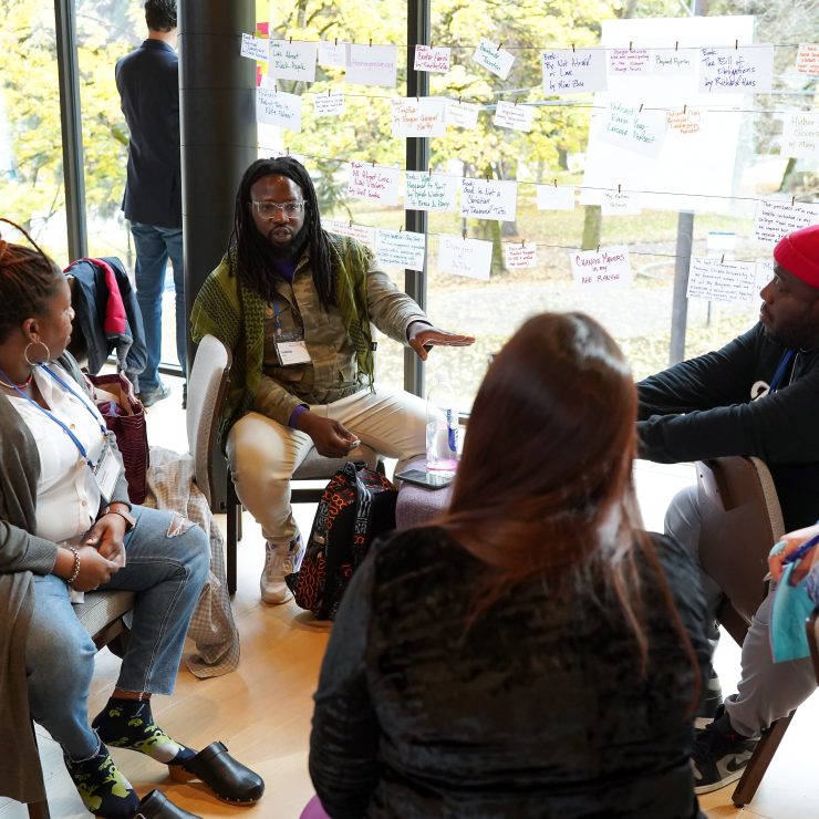 A group photo of Citizen University participants sitting in a circle of chairs, engaging in a discussion.