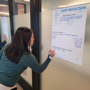 A CSF C24 cohort member writing on a large, white piece of paper. The cohort member is wearing a blue sweater.