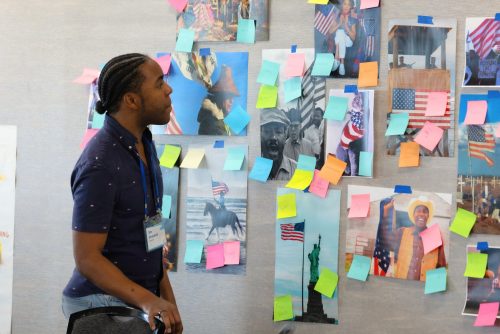 A young person looking at a wall with pictures and stickynotes. 