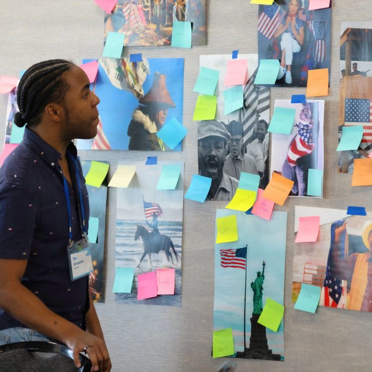 A young person looking at a wall with pictures and stickynotes. 