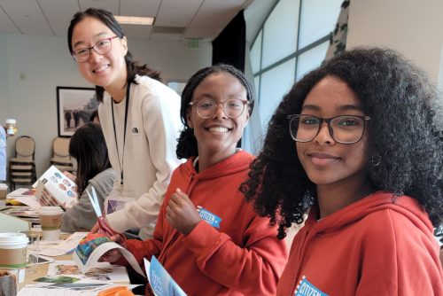 Three young people working on a project at a table and smiling 