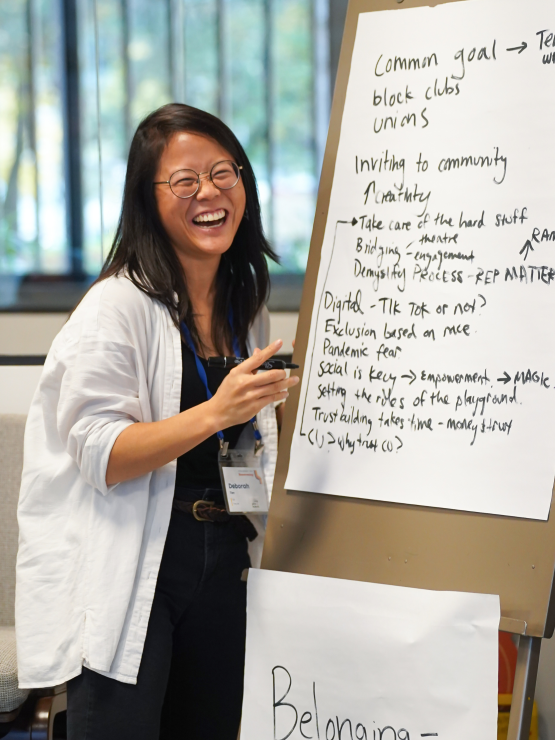 A person seated at a table and smiling while talking to others.