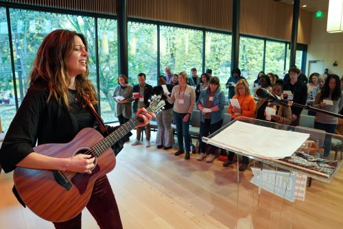 A person playing a guitar on a stage in front of a crowd singing.