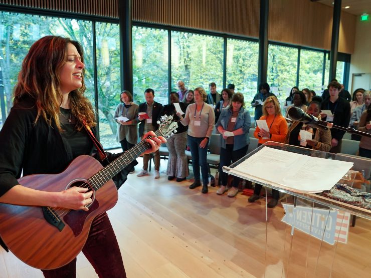 A person playing a guitar on a stage in front of a crowd singing.