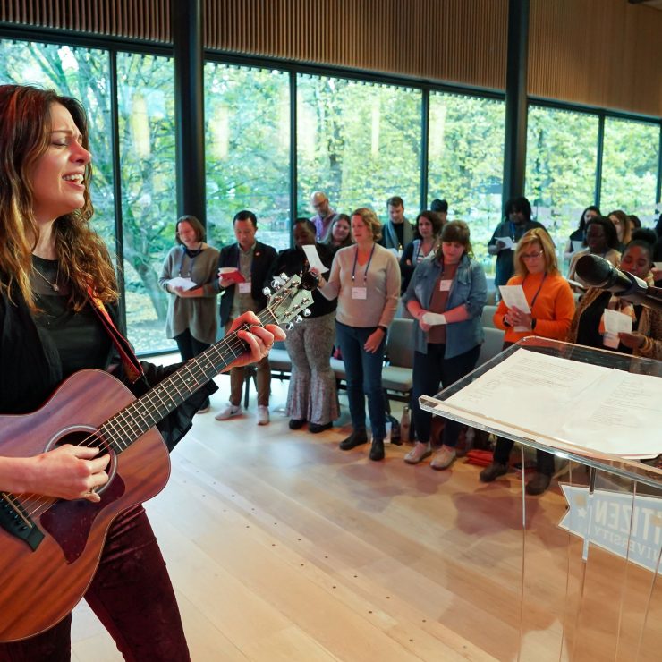 A person playing a guitar on a stage in front of a crowd singing.