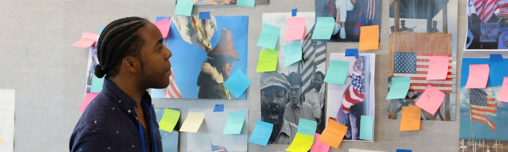 A young person standing in front of a wall looking at pictures and sticky notes.